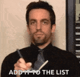 a man in a black shirt and tie is writing on a piece of paper .