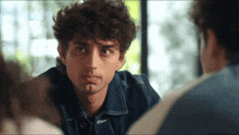 a man with curly hair is wearing a blue jacket