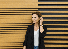a woman wearing a black jacket and a white shirt is standing in front of a wooden wall