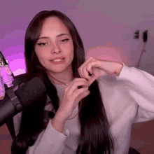 a woman with long hair is sitting in front of a microphone and making a heart shape with her hands