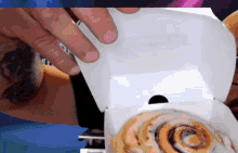 a person with a tattoo on their arm is opening a box of cinnamon rolls
