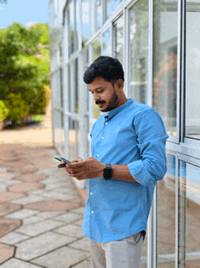a man in a blue shirt is leaning against a window looking at his phone