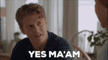 a man is sitting at a table in a living room talking to another man .