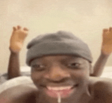 a man wearing a beanie is laying on a bed with his feet up and his mouth open .
