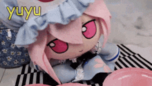 a stuffed doll with pink hair and red eyes is laying on a checkered table cloth with the word yuyu written above her
