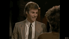 a man in a suit and tie is smiling at a woman in a brown shirt .