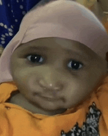a baby wearing a hijab and an orange shirt is making a funny face .