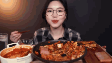 a woman wearing glasses is eating a large plate of food with chopsticks