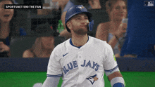 a baseball player wearing a blue jays jersey with a fan in his mouth
