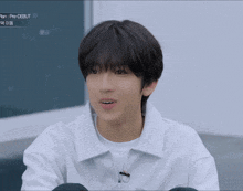 a young man wearing a white shirt is sitting in front of a blackboard that says " plan pre-debut "