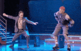 a man in a suit and a man in shorts are dancing on a stage in front of a sign that says suit free
