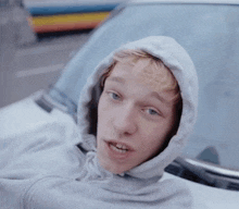a young man wearing a hooded sweatshirt is sitting in a car