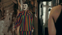 a clown in a rainbow colored outfit with a white face