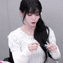 a woman in a white sweater is holding a toothbrush in her hand