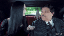 a man in a suit and a woman in a black dress are sitting in a car that says netflix on it
