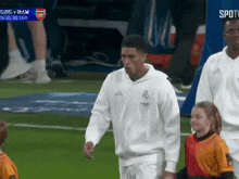 a man wearing a white adidas sweatshirt walks on a soccer field