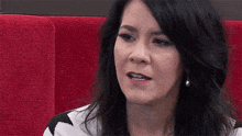 a woman with long dark hair is sitting in a red chair and looking at the camera .