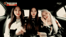 three girls are sitting in the back seat of a car with a mbc live advertisement on the screen behind them