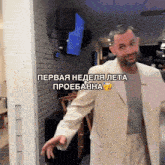 a man in a white suit stands in front of a brick wall with the words " первая неделя лета " above him