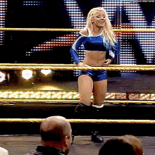 a woman in a blue outfit is standing in a wrestling ring with a crowd watching .