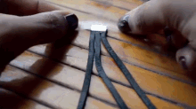 a person is braiding a piece of black leather on a wooden table