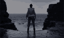 a man is standing on a rocky shoreline looking out over the ocean .