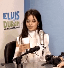 a woman is sitting in front of a microphone in front of a sign that says elvis duran