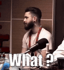 a man with a beard is sitting in front of a microphone with the words `` what ? '' written above him .
