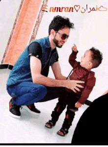 a man kneeling down holding a small child with the name nmran written above him