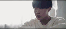 a young man in a white shirt is sitting in front of a window and looking down .