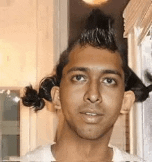 a young man with a mohawk and pigtails is standing in front of a window .
