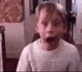 a young boy with a surprised look on his face is standing in a room .