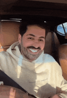 a man with a beard and mustache is smiling while sitting in the back seat of a car .
