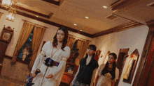 three women are standing in a room with a clock on the ceiling