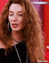 a woman with red curly hair wearing hoop earrings and a necklace
