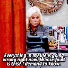 a woman is sitting at a desk talking on a cell phone and says everything in my life is going wrong right now .