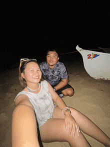 a man and a woman sit on the beach next to a boat that says 2