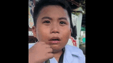 a young boy in a white shirt is making a funny face with his hand on his chin .