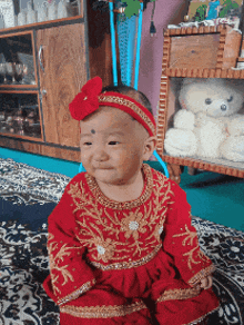 a baby in a red and gold dress with a red flower in her hair
