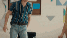 a man in a striped shirt and jeans is standing in a room with a woman .