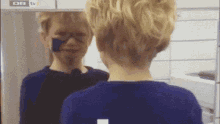 a boy with blue paint on his face is looking at himself in a mirror