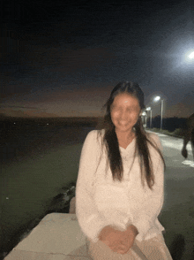 a woman in a white shirt is smiling in front of a lake at night
