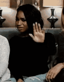 a woman is sitting on a couch with her hand up and making a funny face .