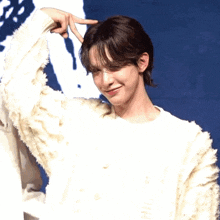 a young man wearing a white sweater making a peace sign