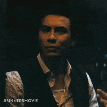 a man in a suit and vest is standing in a dark room and looking at the camera .