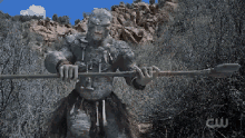 a statue of a giant holding a spear in front of a hill .