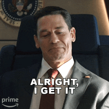 a man in a suit and tie is sitting in a chair and says " alright i get it "
