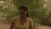 a woman in a yellow t-shirt is standing next to a tree in the woods .