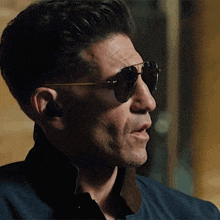 a man wearing sunglasses and a blue jacket looks to the side
