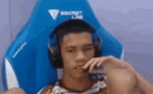 a young man is sitting in a blue gaming chair wearing headphones and eating a snack .